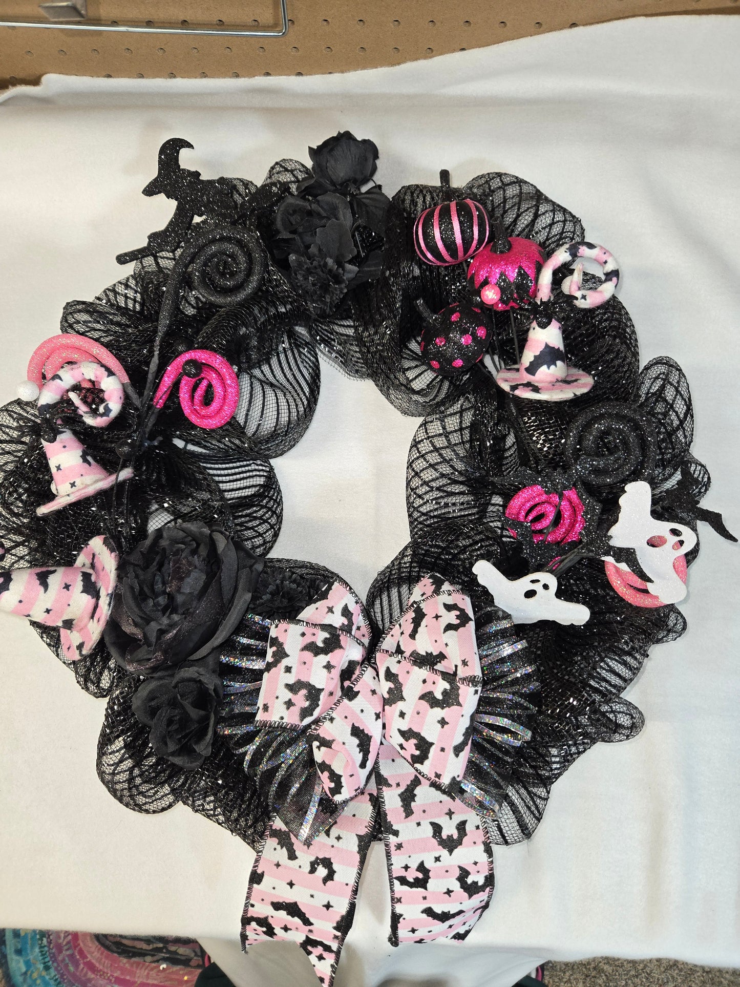 Halloween-themed wreath with black mesh, pink ribbons, and ghost decorations on a white background.