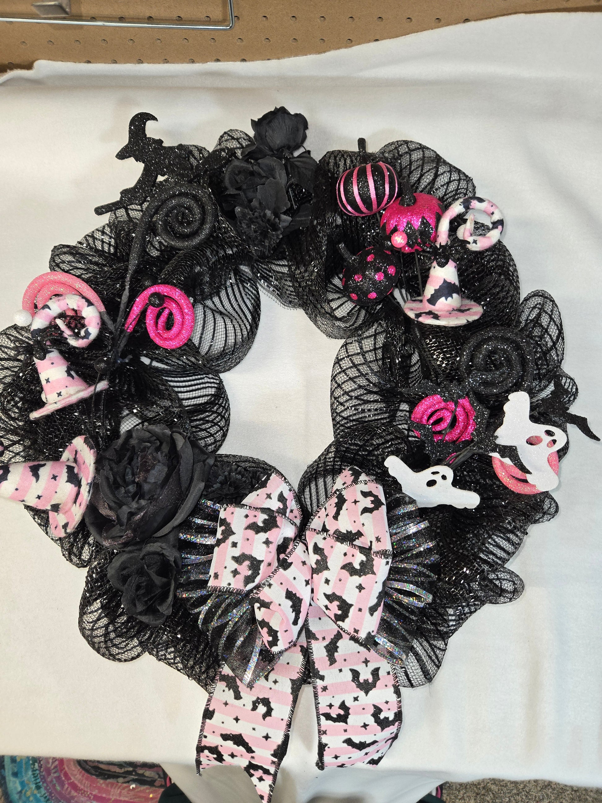 Halloween-themed wreath with black mesh, pink ribbons, and ghost decorations on a white background.