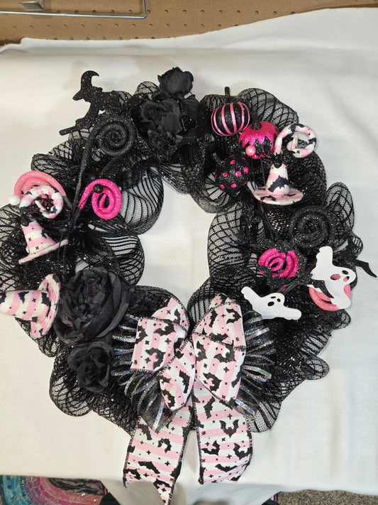 Halloween-themed wreath with black mesh, pink ribbons, and ghost decorations on a white background.